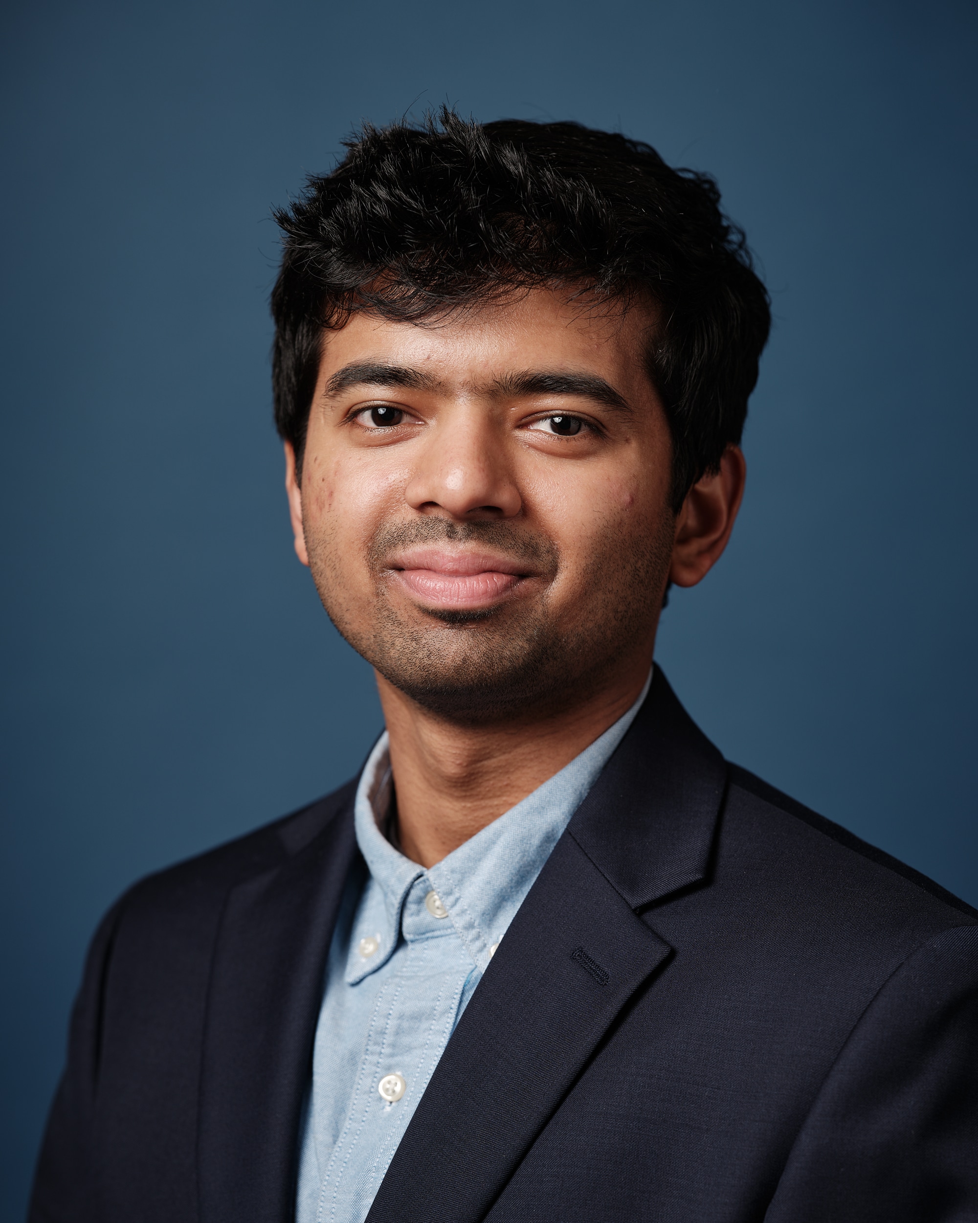 Headshot of Aniruddha Doke with dark colored suit, blue shirt and blue background.