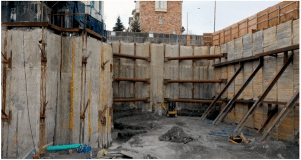 Shored excavation with steel bracing and compact excavator at 935 Eglinton Avenue West construction site.