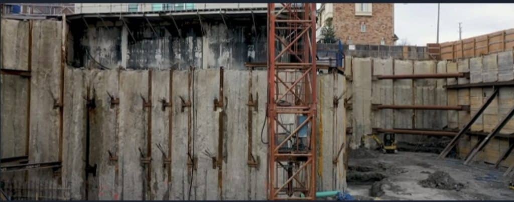 Close-up view of excavation shoring at 935 Eglinton Avenue West, showing vertical concrete walls, steel reinforcements, and excavation equipment.